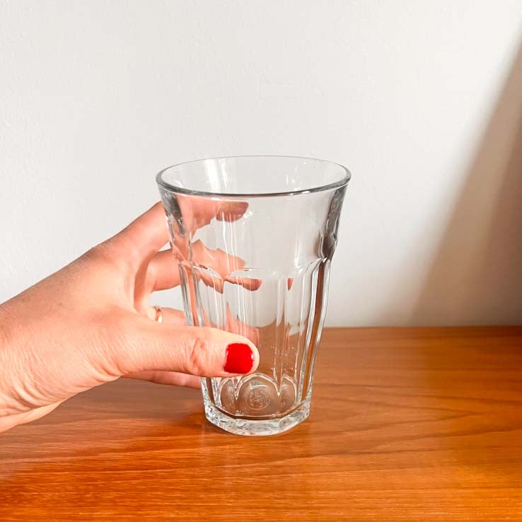 Hand holding a clear Duralex Picardie Highball glass on a wooden surface with a white background