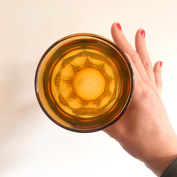 Hand holding a transparent amber-colored glass bowl against a light background