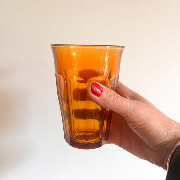 Hand holding an French amber Picardie Duralex glass mug against a plain background
