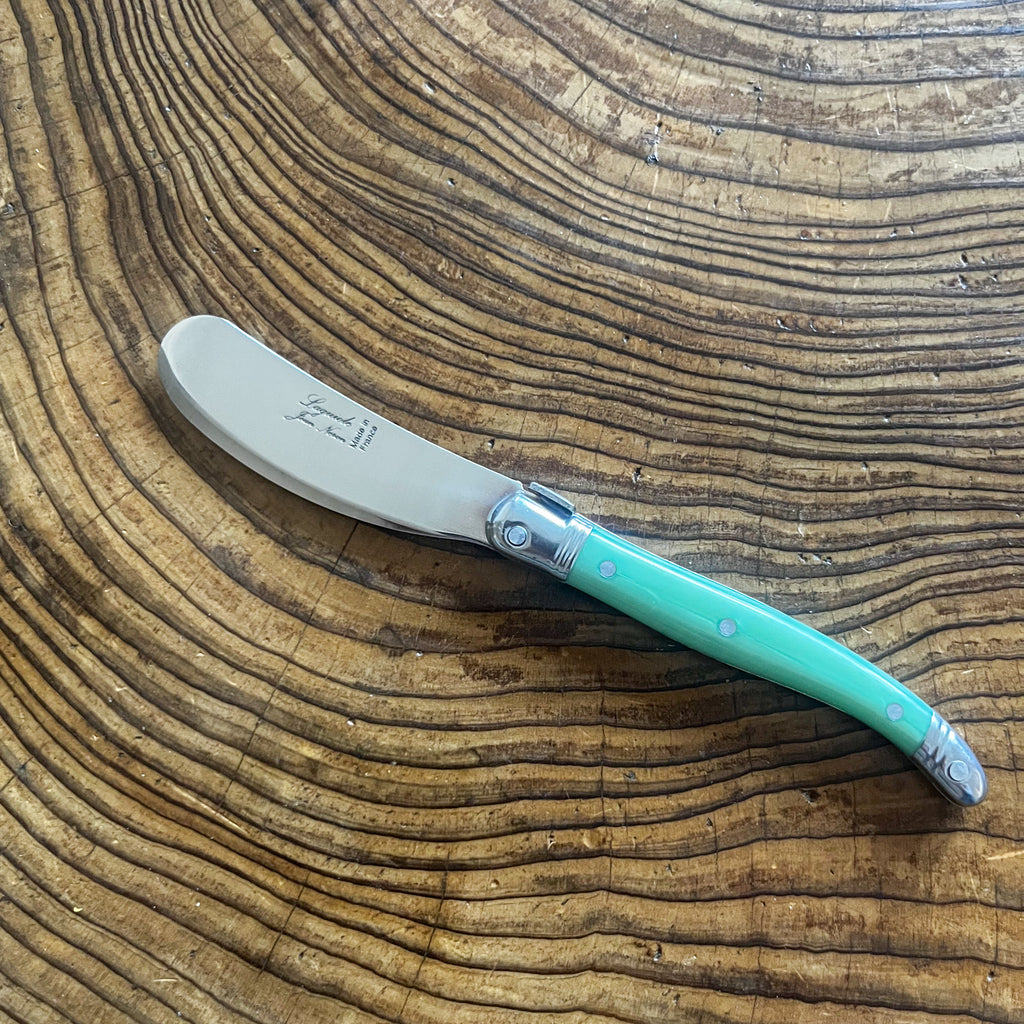 A Laguiole butter knife with a pastel green handle and stainless steel blade, placed on a wooden surface.