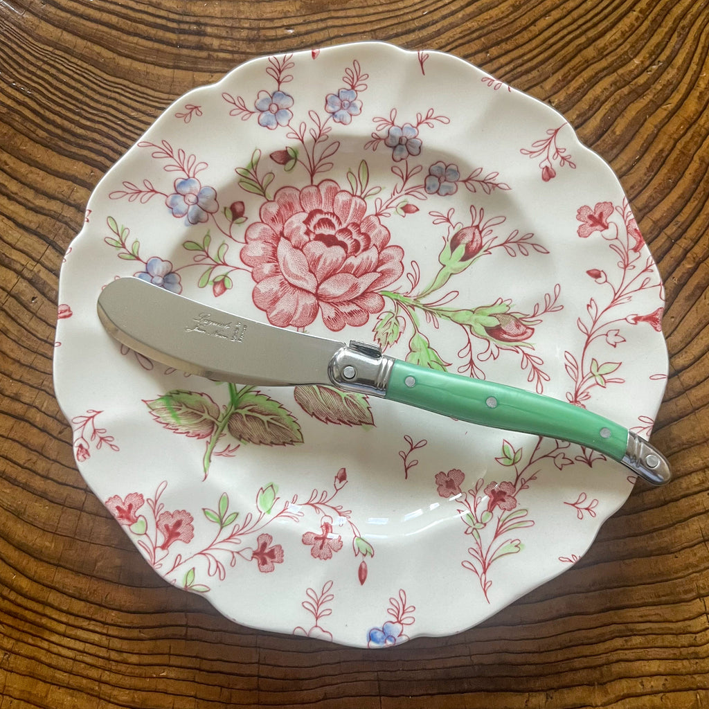 Floral-patterned plate with a Laguiole Butter knife on a wooden surface Clementine Boutique