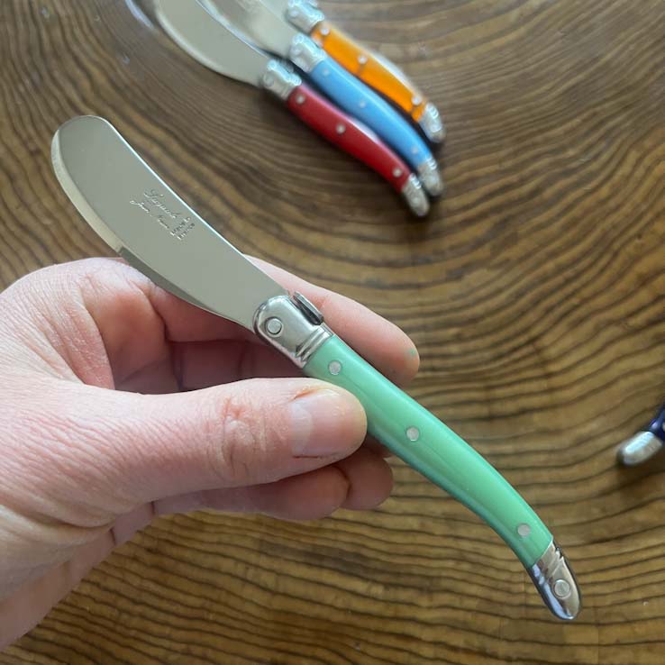A Laguiole butter knife with a pastel green handle and stainless steel blade, placed on a wooden surface.