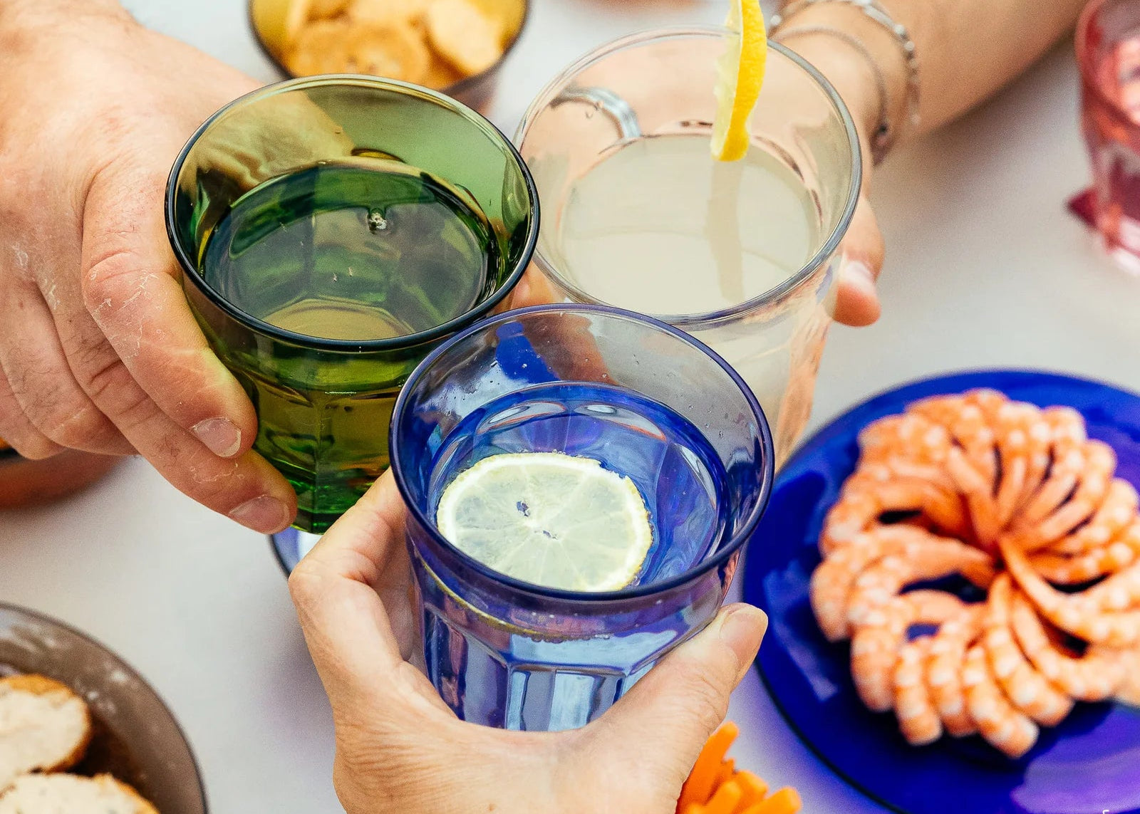 Three people holding glasses of lemon-infused drinks with snacks on a table.